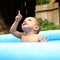 Happy cute baby boy in blue inflating pool pointing up