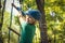 Happy cute boy playing at adventure park, holding ropes and climbing wooden stairs