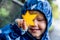 Happy cute caucasian little boy toddler preschooler wearing blue raincoat jacket holding yellow maple leaf on a rainy autumn day.