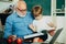 Happy cute clever boy and old tutor with book. Funny little child having fun on blackboard background. A grandfather and