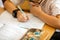 Happy cute clever boy is sitting at a desk in a glasses with raising hand. Child is ready to answer with a blackboard on a