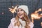Happy cute girl in winter hat posing with sparkler. Outdoor shot of interested blonde woman having fun in holidays..