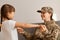 Happy cute little girl with braids wearing white t shirt holding mother hands, military woman arrived from army, sitting on sofa