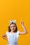 Happy cute little girl on a yellow background. The child points to an empty copy space