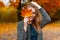 Happy cute young attractive woman with a smile in a fashionable coat is standing in the park and covering her face