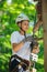 Happy, cute, young boy in white t shirt and helmet having fun and playing at adventure park, holding ropes