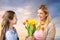 Happy daughter giving flowers to mother over sky