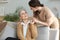 Happy daughter hugging older mother, standing behind sofa in living room, enjoying tender moment at home