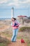 Happy delightful active young woman holding little chihuahua dog in animal clothes near ocean coast with lighthouse