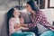 Happy delightful aunt wearing checkered shirt and jeans is tickling her cute lovely and laughing niece, they are sitting on