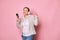 Happy delightful pregnant woman in wireless headphones, holding mobile phone, dancing, isolated on pink background
