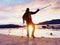 Happy disabled man on beach holding his forearm crutches above head, warm sunset