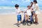 Happy disabled senior elderly woman in wheelchair spending time together with her family on tropical beach. Asian grandma,