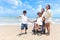 Happy disabled senior elderly woman in wheelchair spending time together with her family on tropical beach. Asian grandma,