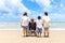 Happy disabled senior elderly woman in wheelchair spending time together with her family on tropical beach from behind. Asian