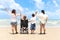 Happy disabled senior elderly woman in wheelchair spending time together with her family on tropical beach from behind. Asian