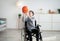 Happy disabled teenager playing with basketball, sitting in wheelchair at home