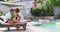 Happy diverse couple in love playing guitar, their friend jumping into swimming pool at pool party