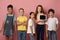 Happy diverse schoolchildren holding tablet computer with empty screen on pink background, mockup for design