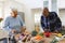 Happy diverse senior couple slicing butternut squash, preparing vegetables in kitchen