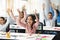 Happy diverse small schoolchildren raising hands at classroom