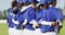 Happy diverse team of female baseball players standing on field with arms around each other