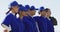 Happy diverse team of female baseball players standing in line with arms around each other singing