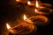 Happy Diwali - many Terracotta diya or oil lamps arranged over clay surface or ground in one line or curved or zigzag form, select