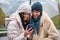 Happy dominican lesbian couple using the phone in a rainy day of winter.