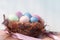 Happy Easter. Colorful Easters eggs in a nest with feathers and a chalk board on a wooden stump.