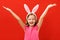 Happy easter. Cute little girl in bunny ears raised her hands up. Close-up baby on a colored red background