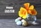 Happy Easter greeting card.Yellow-orange Eschscholzia or California Poppy flowers in a glass vase and quail eggs on a wooden table