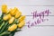 Happy easter hand lettering calligraphy text. Yellow tulips bunch on white wooden planks rustic barn rural table background.