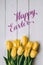 Happy Easter hand lettering calligraphy text. Yellow tulips bunch on white wooden planks rustic barn rural table background.