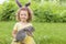 Happy Easter kid. little girl with very peri ears, small rabbit, grey bunny hunting for colorful eggs on green grass. spring holid