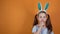 Happy Easter. A little Caucasian girl with bunny ears on her head brings her finger to her lips and asks for silence.