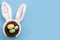 Happy easter and spring meme concept with adorable bunny ears on a bird nest with colorful eggs against a baby blue background