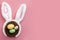 Happy easter and spring meme concept with adorable bunny ears on a bird nest with colorful eggs against a bright pink background