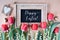 Happy Easter, text on blackboard on light wood with decorative ribbon and heart tag, quail eggs and spring flowers - red tulips,