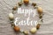 Happy Easter text on Easter eggs and spring flowers wreath on rustic linen, flat lay, handwritten sign. Beautiful stylish greeting