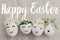 Happy Easter text on eggs with cute funny faces in floral crowns on rustic fabric with spring flowers and blossom, handwritten