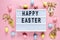 Happy Easter text on lightbox on pink pastel paper background with yellow, pink, blue eggs and bunnies. Bright template for Easter