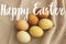 Happy Easter text on modern yellow and brown easter eggs on rustic linen cloth, handwritten sign. Beautiful stylish greeting card