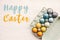 Happy Easter text sign on stylish easter eggs in carton tray on white wooden table, flat lay. Modern colorful easter eggs painted