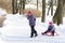 Happy elder sister pulling her young sister on the sleds in snowy winter park