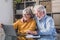 Happy elderly 60s couple sit rest on couch at home pay household expenses online on computer, smiling mature 50s husband and wife