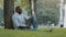 Happy elderly African black businessman wearing wireless headphones sitting on grass in city park listen music in