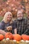 Happy elderly baby boomer couple poses in an autumn scene with a dog and pumkins