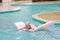 Happy elderly caucasian swimming and playing rubber boat in swimming pool during retirement holiday with relaxation and smiling