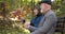 Happy elderly husband and wife communicate and relax on a bench in the central park of the city and look at an autumn